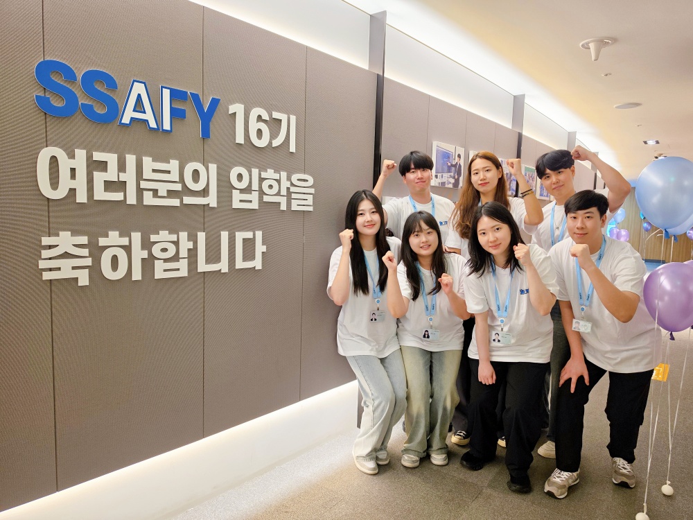 SSAFY 16기 입학생들이 환영 문구 앞에서 주먹을 쥐고 기념 촬영을 하고 있다.