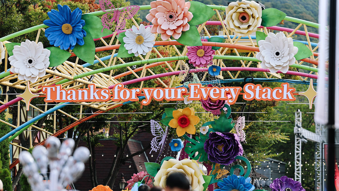 알록달록한 조형 꽃과 나비로 장식된 아치형 구조물에 'Thanks for your Every Stack' 문구가 걸려 있다.