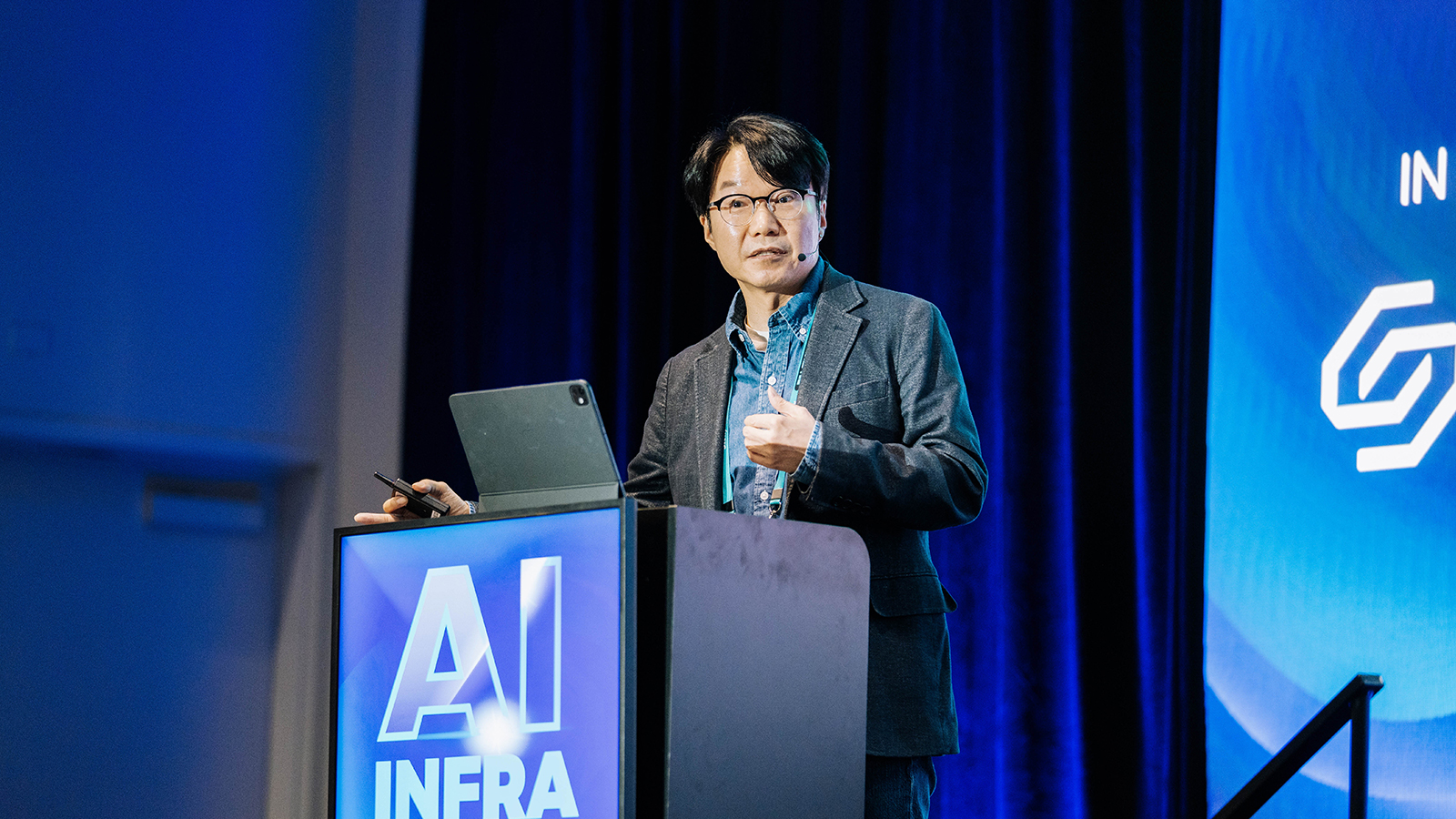 연사가 'AI INFRA' 로고가 표시된 연단에서 마이크를 착용하고 발표하는 모습.