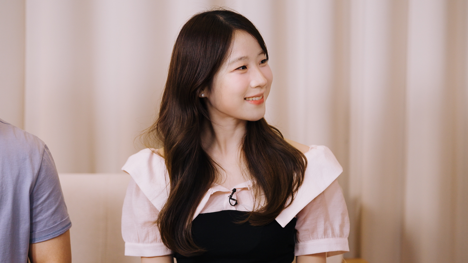 마이크를 착용한 여성이 인터뷰 중 밝게 미소 짓고 있다.