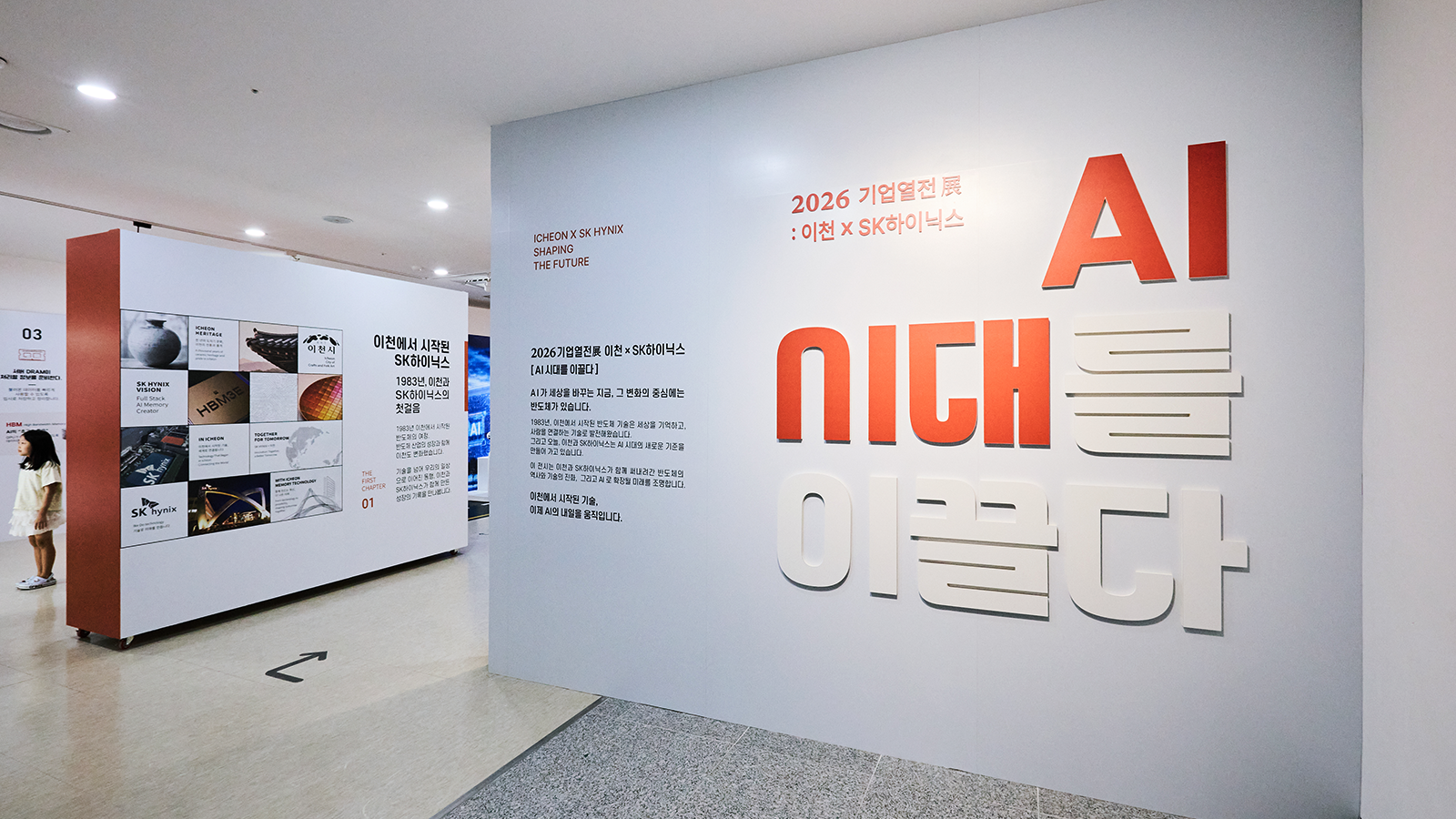 '2026 기업열전展: 이천×SK하이닉스'와 'AI 시대를 이끌다' 문구가 벽면에 전시된 SK하이닉스 이천 전시관 입구 모습.