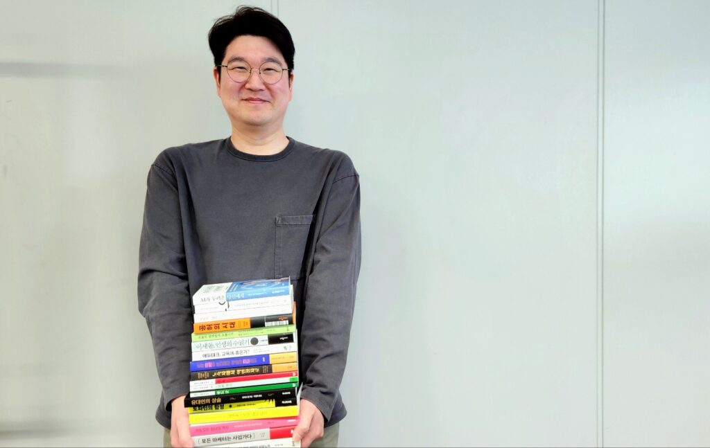 전병욱 멘탯 대표가 여러 권의 책을 품에 안고 환하게 웃으며 서 있는 모습.