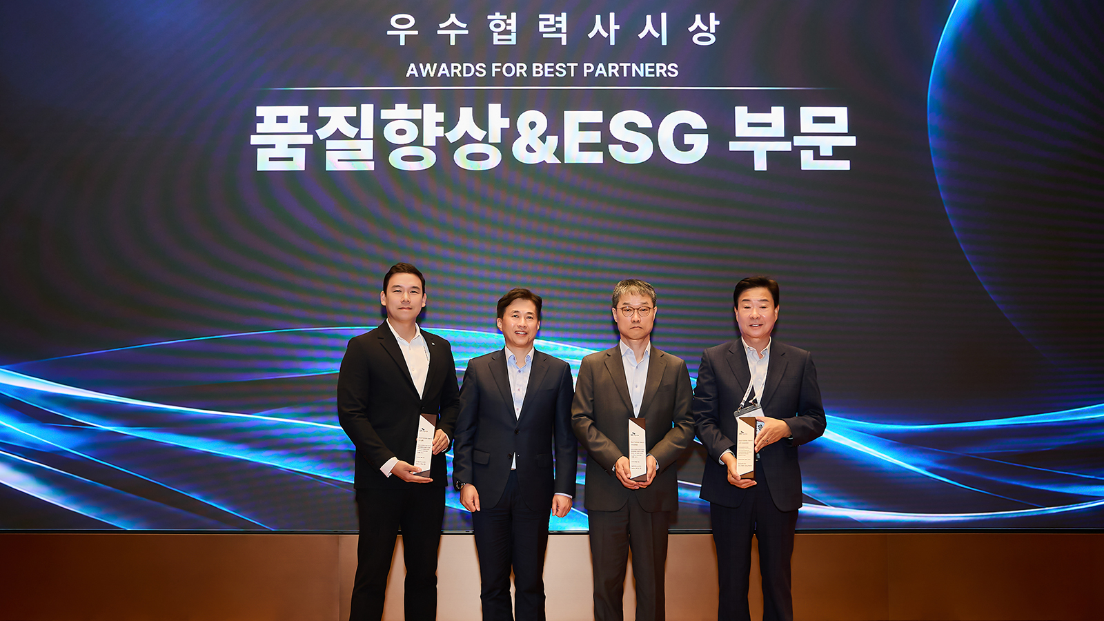 SK하이닉스 우수협력사 시상식에서 품질향상&ESG 부문 수상자들이 트로피를 들고 무대에서 기념 촬영하고 있다.