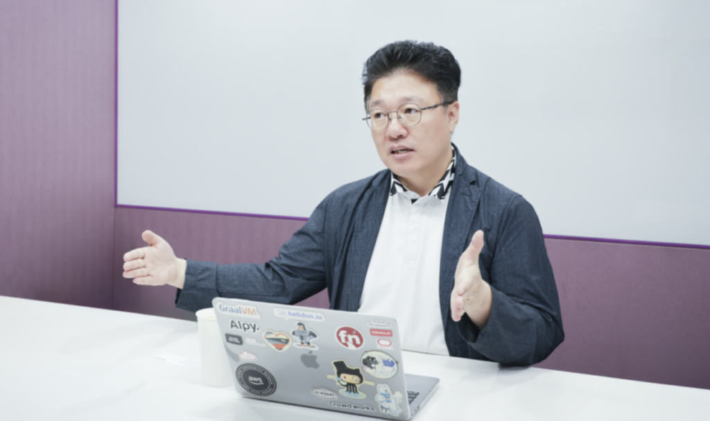 양수열 크라우드웍스 CAIO가 스티커로 장식된 노트북 앞에서 두 손을 펼치며 피지컬 AI와 데이터에 대해 설명하고 있다.