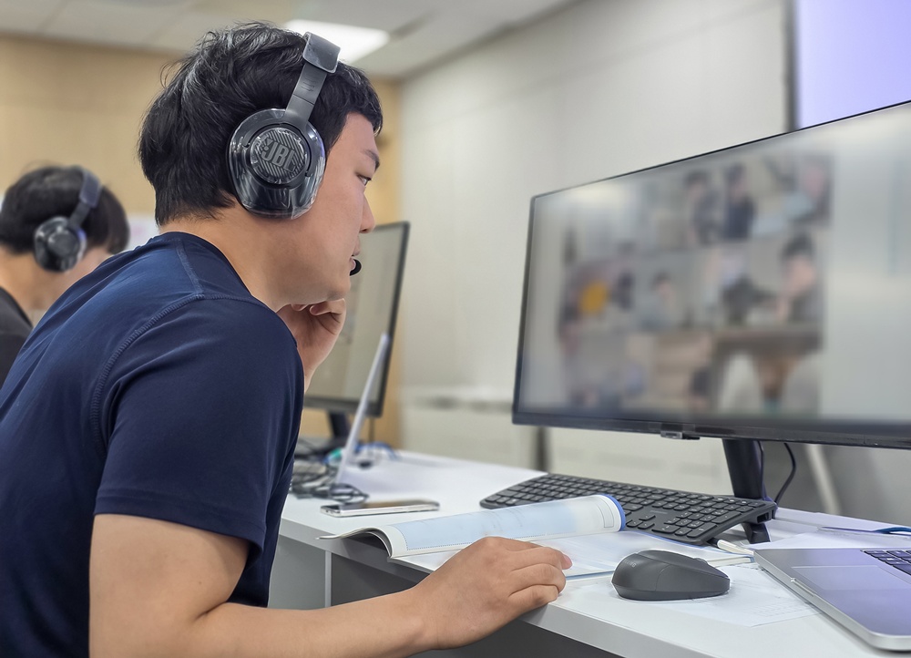 헤드셋을 착용한 남성이 모니터 화면 속 화상회의를 보며 업무를 진행하고 있다.