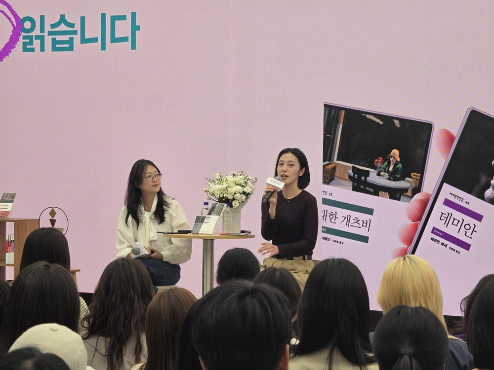 마이크를 든 강연자가 청중 앞에서 이야기하고 있으며, 스크린에는 '위대한 개츠비'와 '데미안' 책 표지가 띄워져 있다.