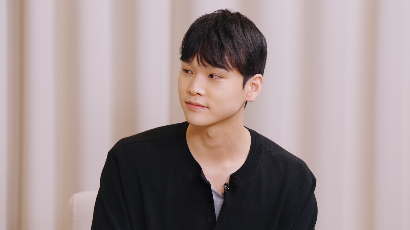 검은색 상의를 입은 남성이 인터뷰 중 옆을 바라보고 있다.