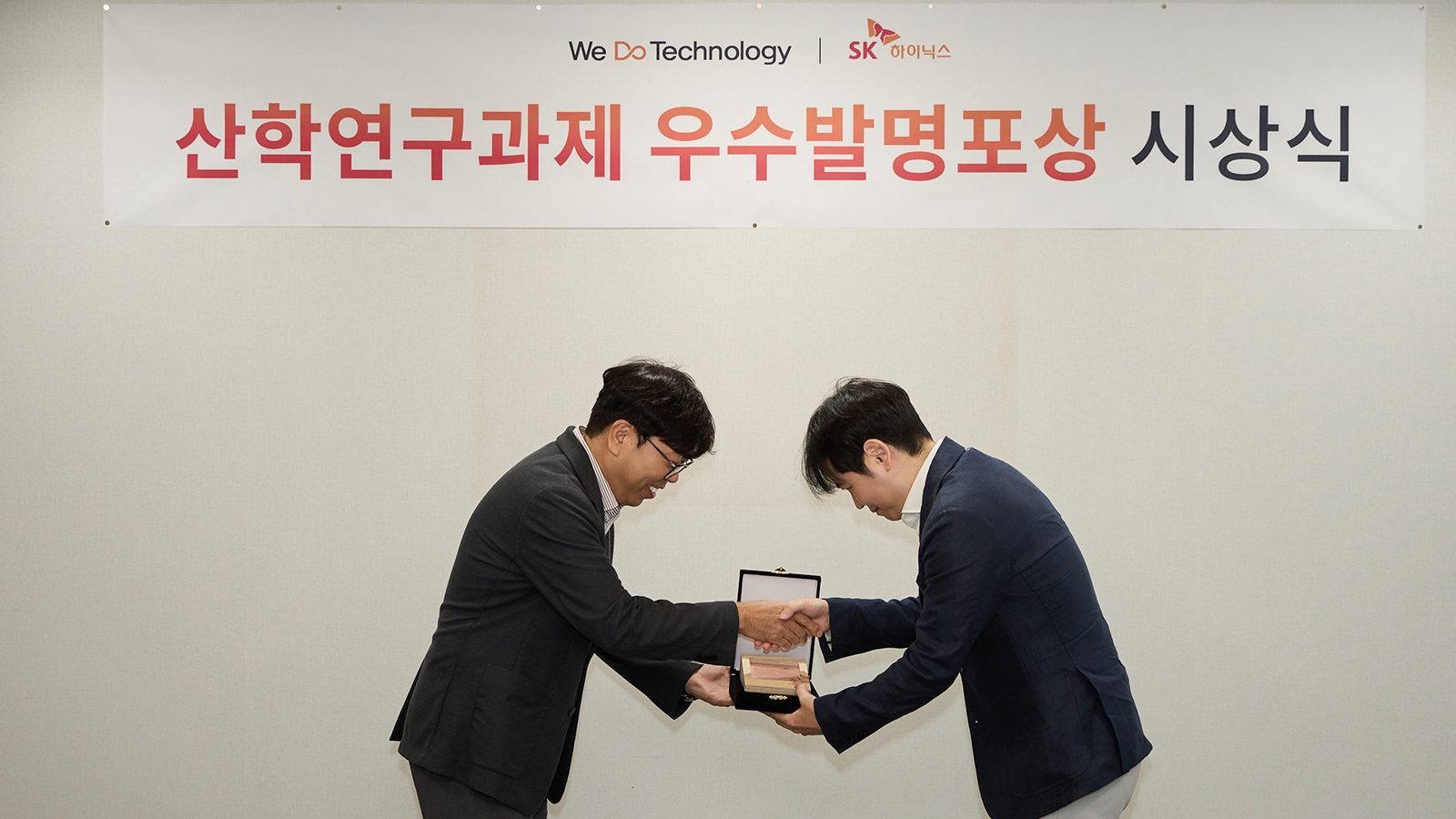 SK하이닉스 산학연구과제 우수발명포상 시상식에서 관계자가 수상자에게 상패를 전달하며 악수하는 모습.