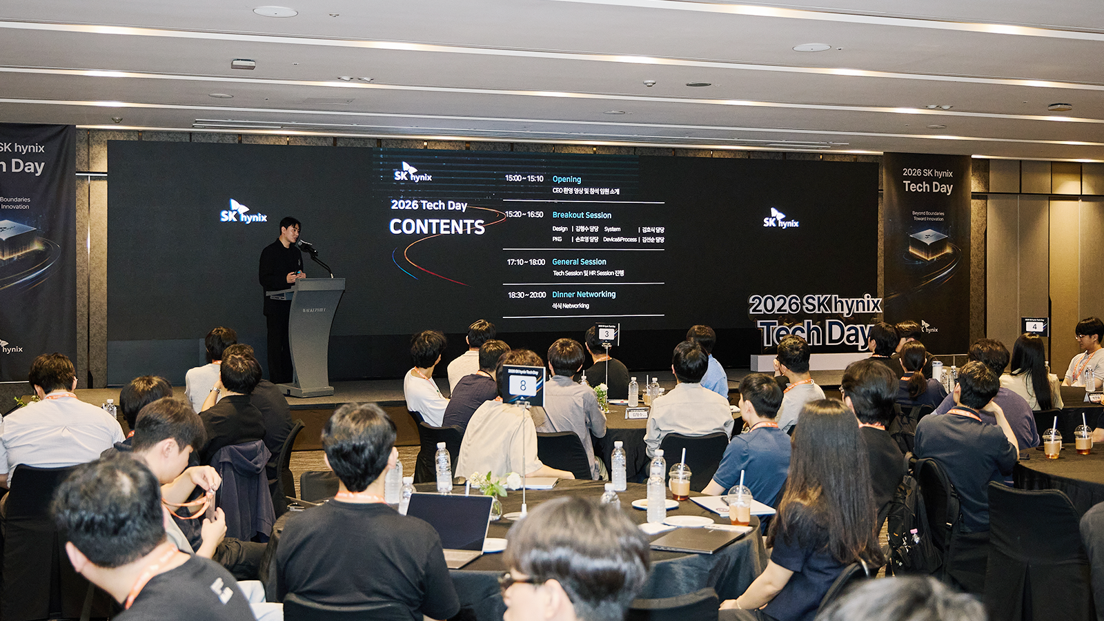 SK하이닉스가 개최한 '2026 Tech Day' 행사에서 발표자가 무대에서 프로그램 일정을 소개하고 참석자들이 경청하고 있다.