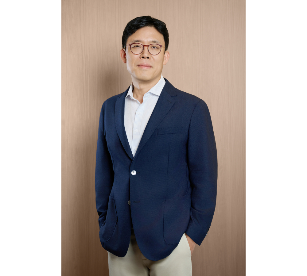 안경을 쓴 남성이 네이비 재킷 차림으로 정면을 응시하며 서 있는 인물 사진.