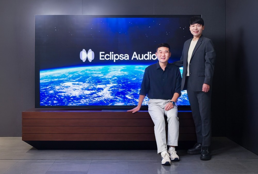 Eclipsa Audio 로고가 표시된 대형 TV 앞에서 관계자 두 명이 포즈를 취하고 있다.