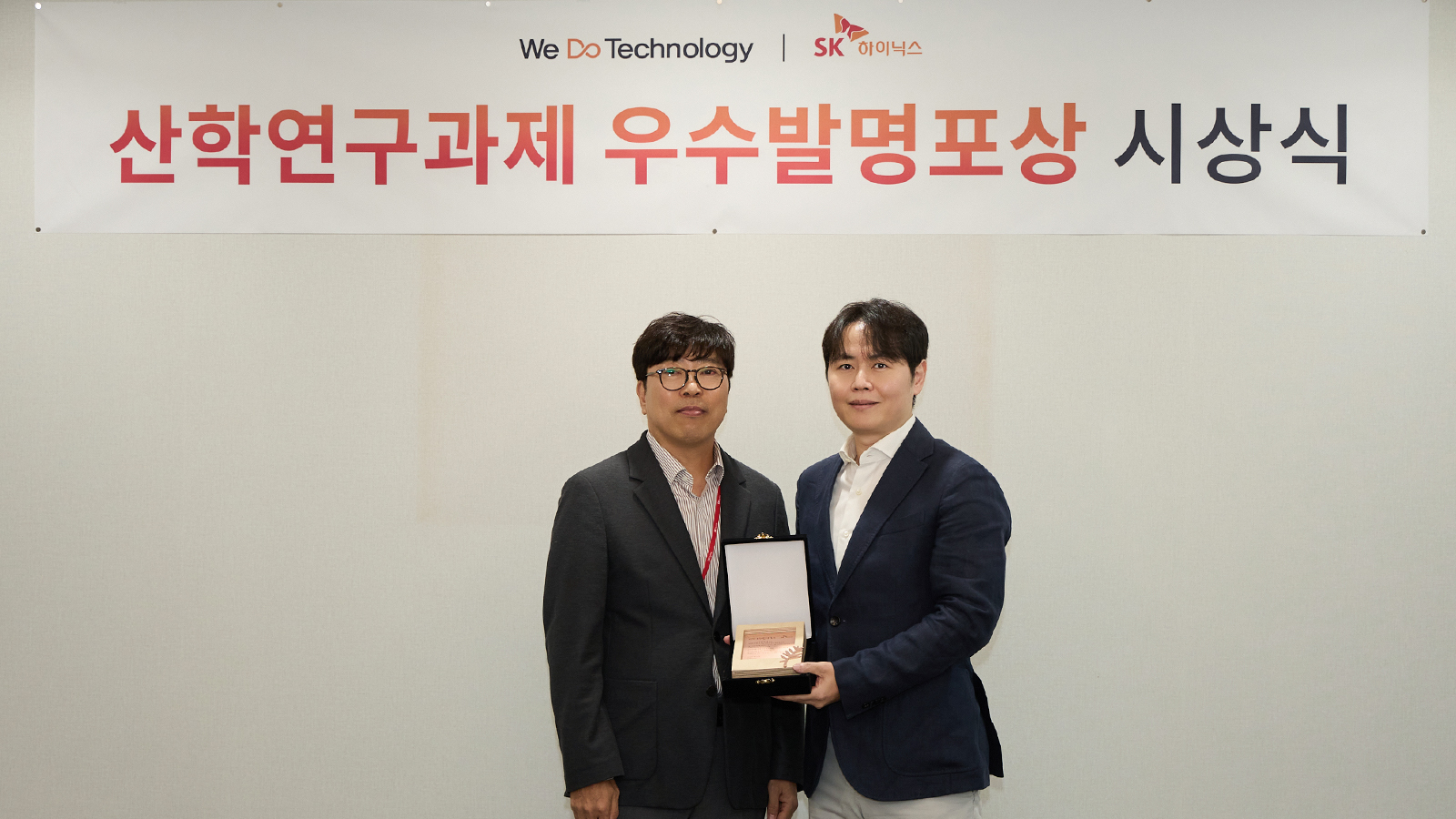 SK하이닉스 산학연구과제 우수발명포상 시상식에서 관계자 두 명이 상패를 함께 들고 기념 촬영하고 있다.