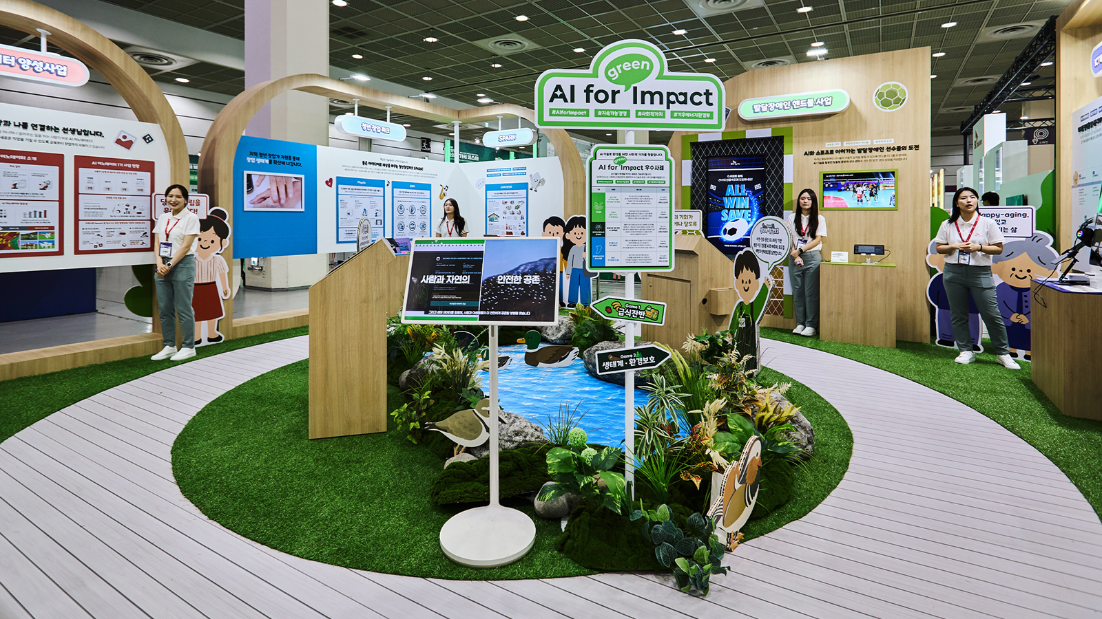 'AI for Impact' 전시 부스에 인공 연못과 생태계 조형물이 설치돼 있고 안내 요원들이 관람객을 맞이하고 있다.