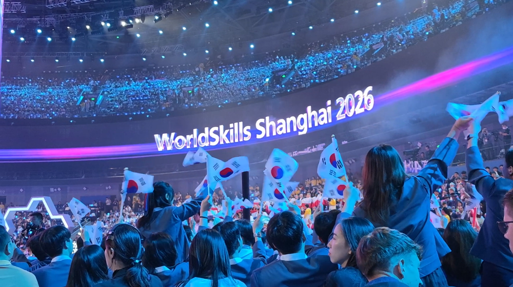 대형 전광판에 'WorldSkills Shanghai 2026' 문구가 떠 있고, 관중석에서 한국 선수단이 태극기를 흔들며 환호하고 있다.