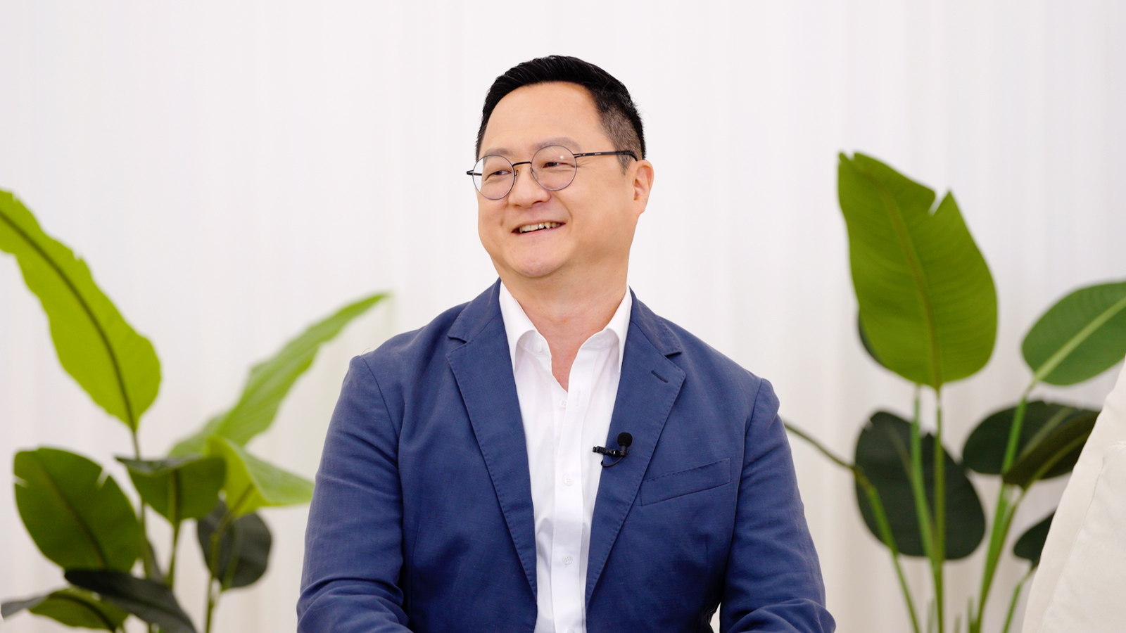 안경을 쓴 남성이 마이크를 착용한 채 인터뷰에서 웃으며 이야기하고 있다.
