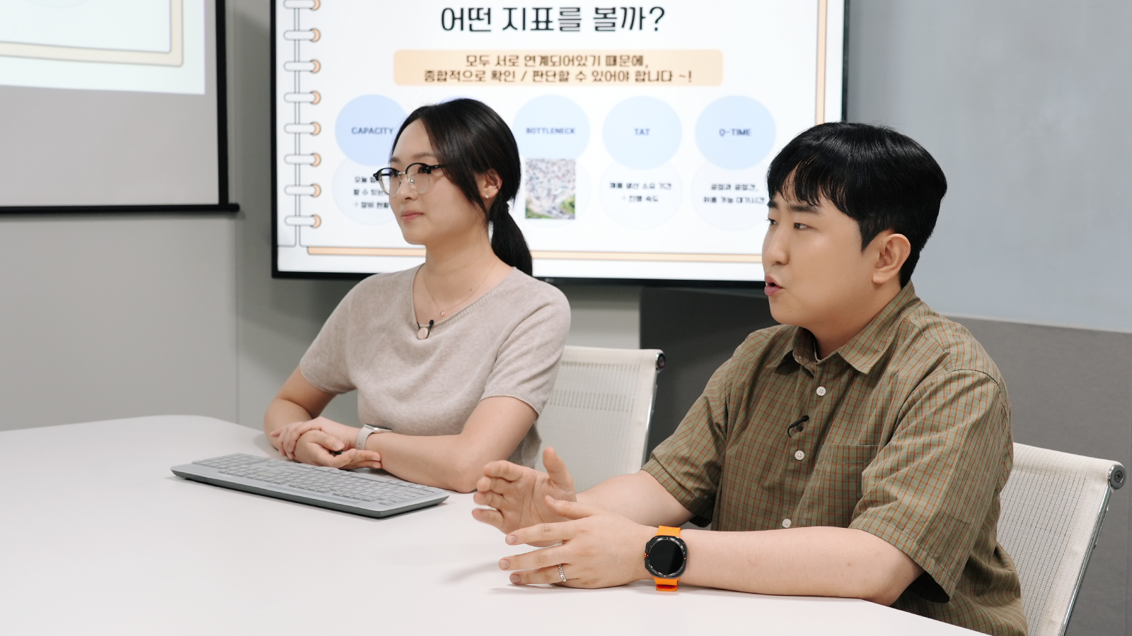 SK하이닉스 직원 두 명이 회의실에서 생산 지표 화면을 보며 양산관리 업무에 대해 설명하고 있다.
