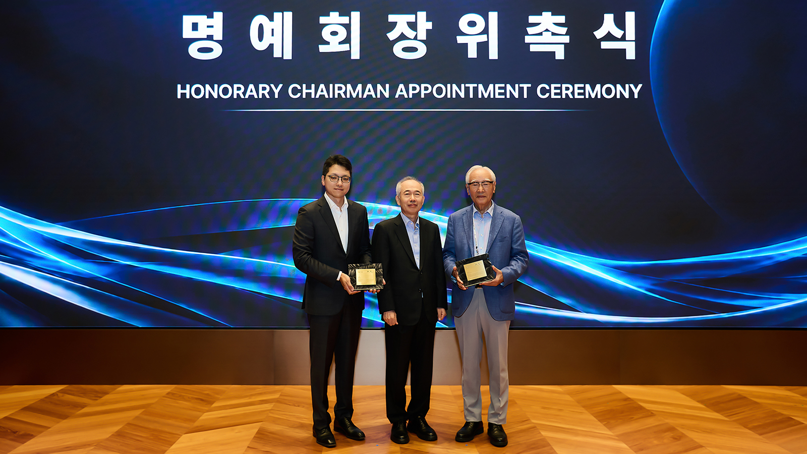 명예회장 위촉식에서 관계자 세 명이 명패를 들고 기념 촬영하는 모습, SK하이닉스 2026 파트너스데이 행사 현장.