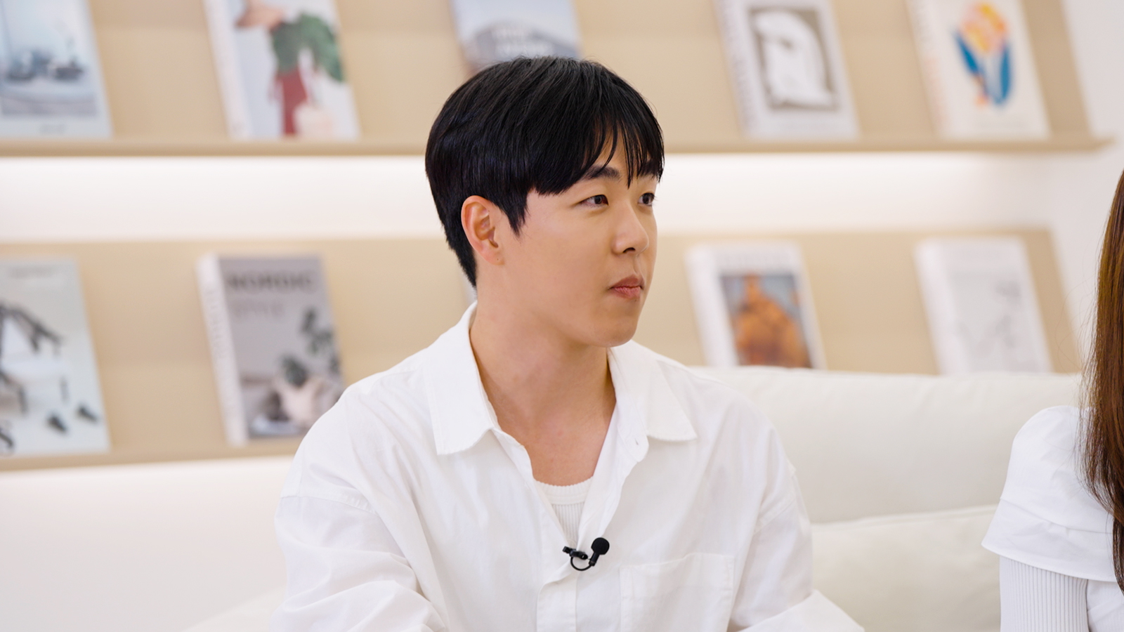 흰색 셔츠를 입은 남성이 인터뷰 중 옆을 바라보며 이야기하고 있다.